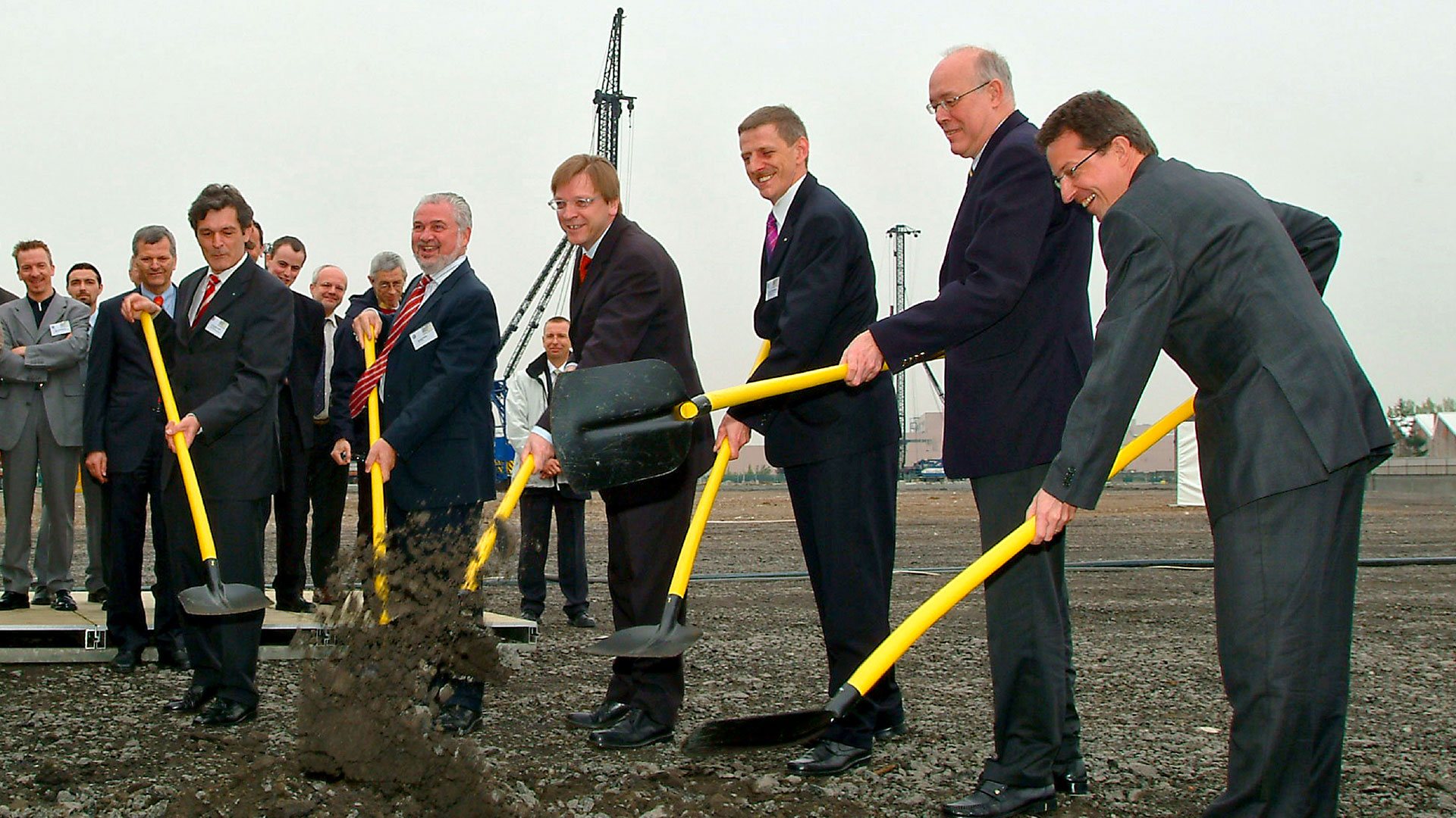 An empty lot with 6 people in suits holding yellow shovels