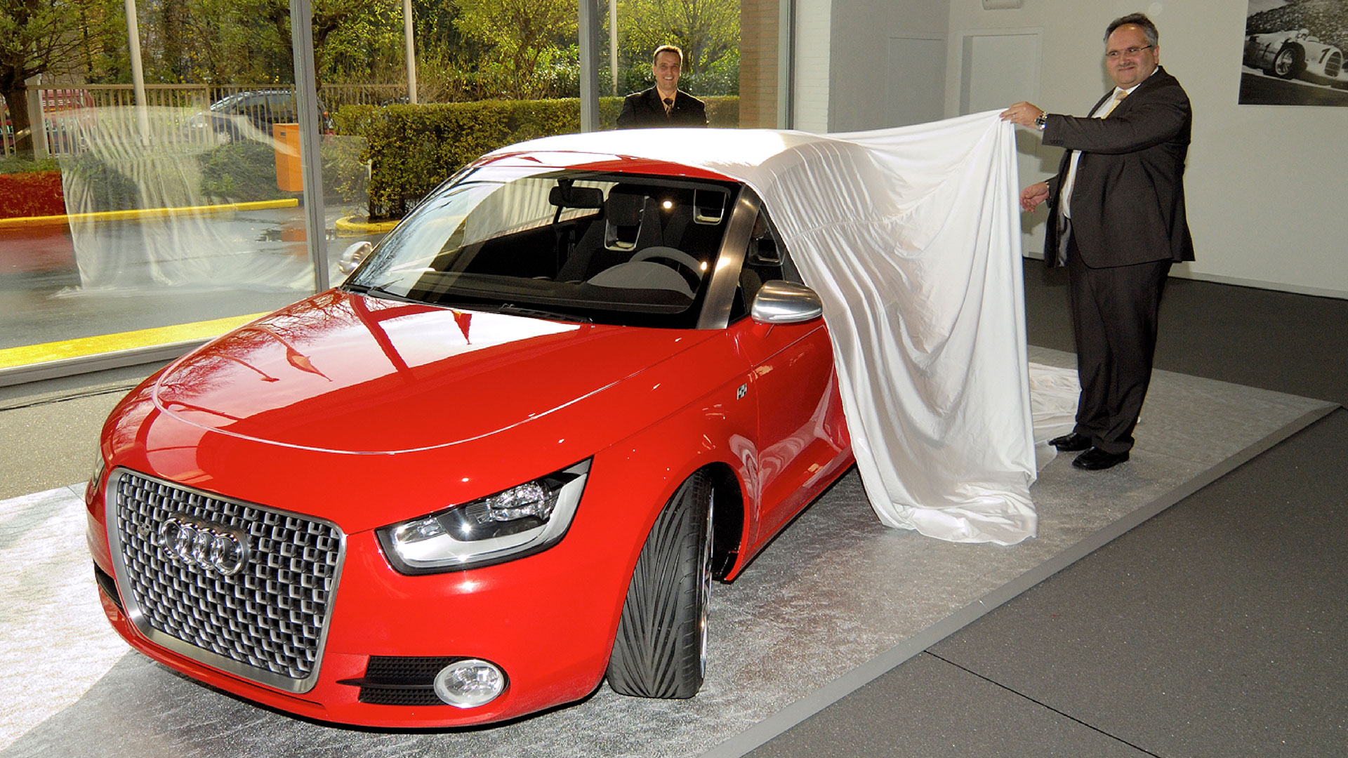 Ann old red Audi model being unveiled by 2 people in the showroom